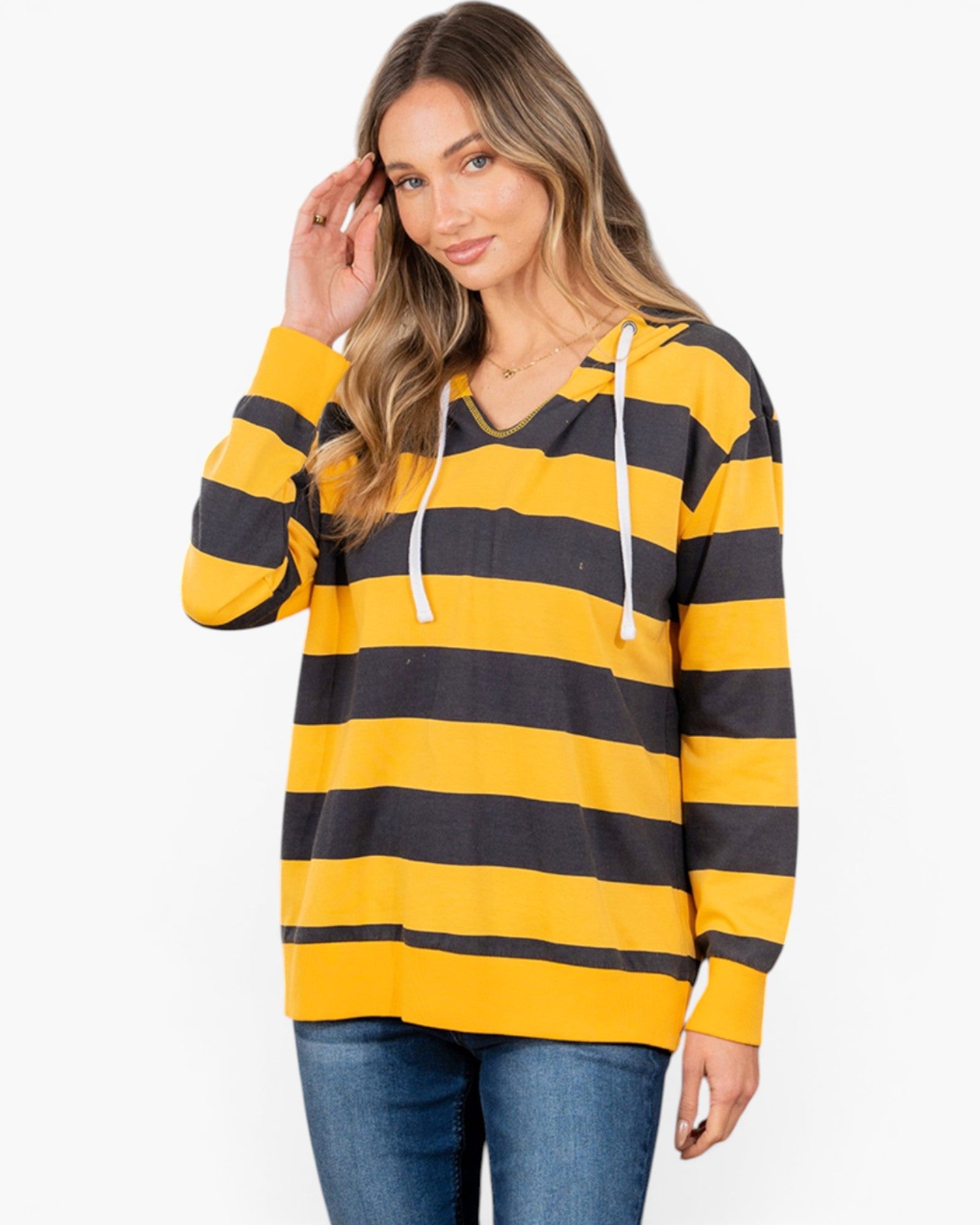 A woman wearing a yellow and black horizontally striped long-sleeve hoodie with white drawstrings, paired with blue jeans, against a plain white studio background.
