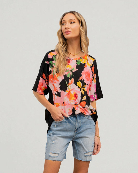 Woman wearing a black t-shirt with colorful floral pattern and denim shorts on a plain background