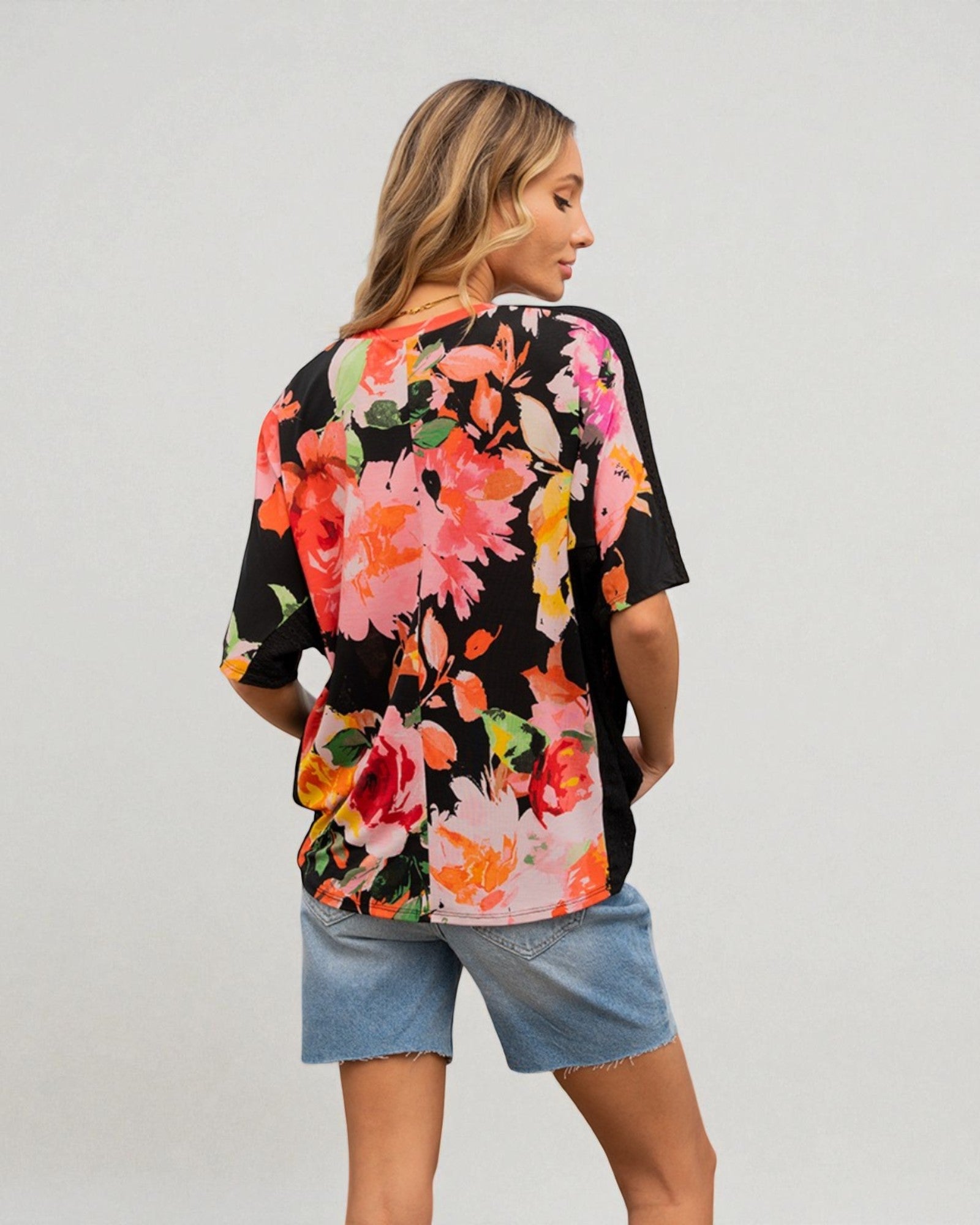 Woman wearing a black floral blouse with denim shorts on a plain background