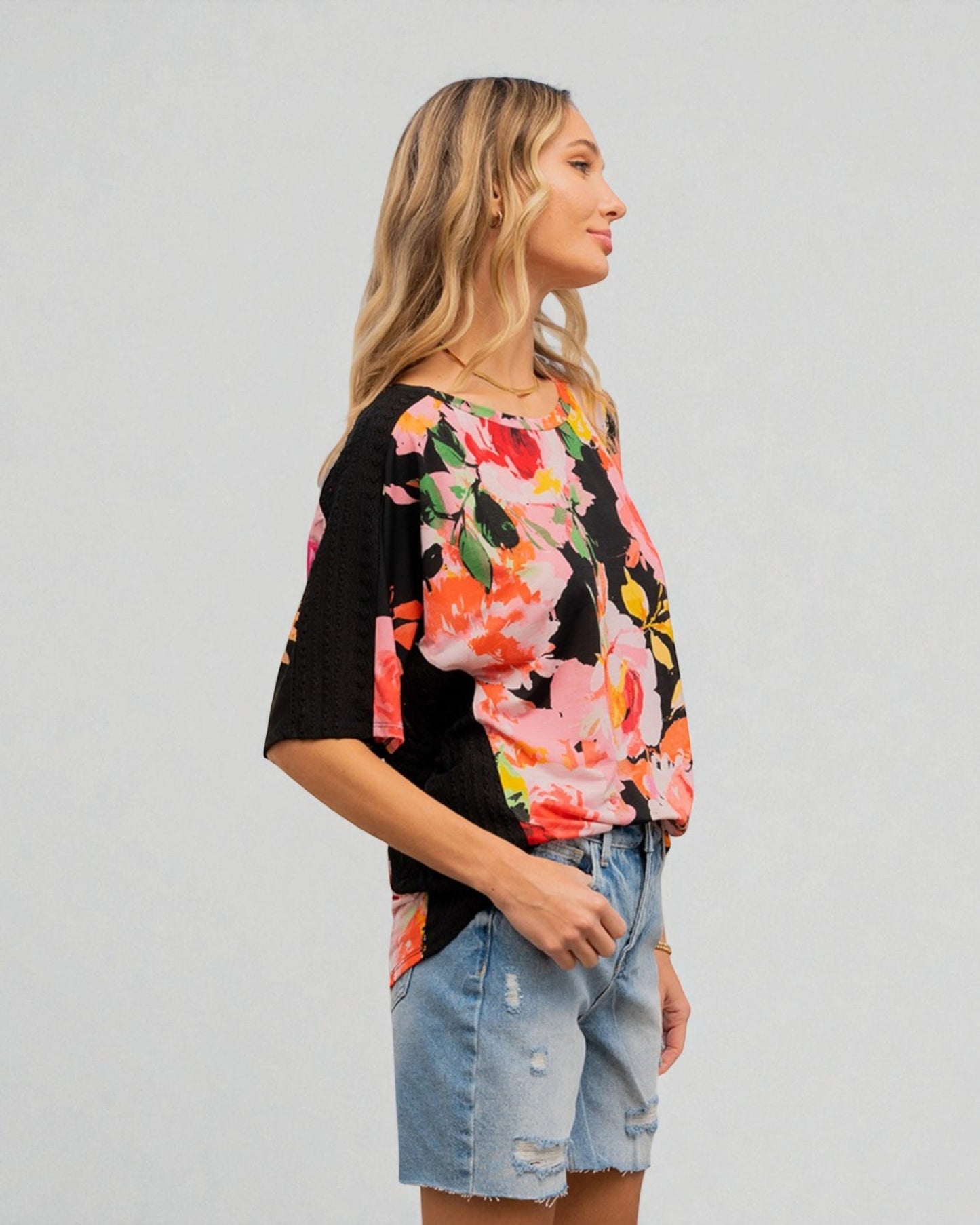 Woman wearing a black floral top and denim shorts on a plain background