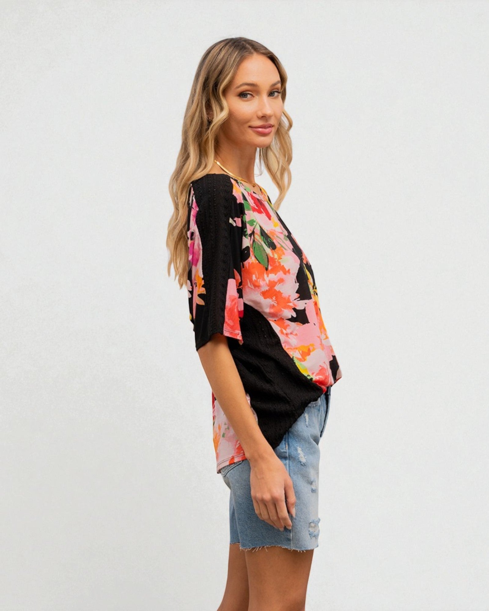 Woman wearing a black floral blouse with denim shorts on a white background