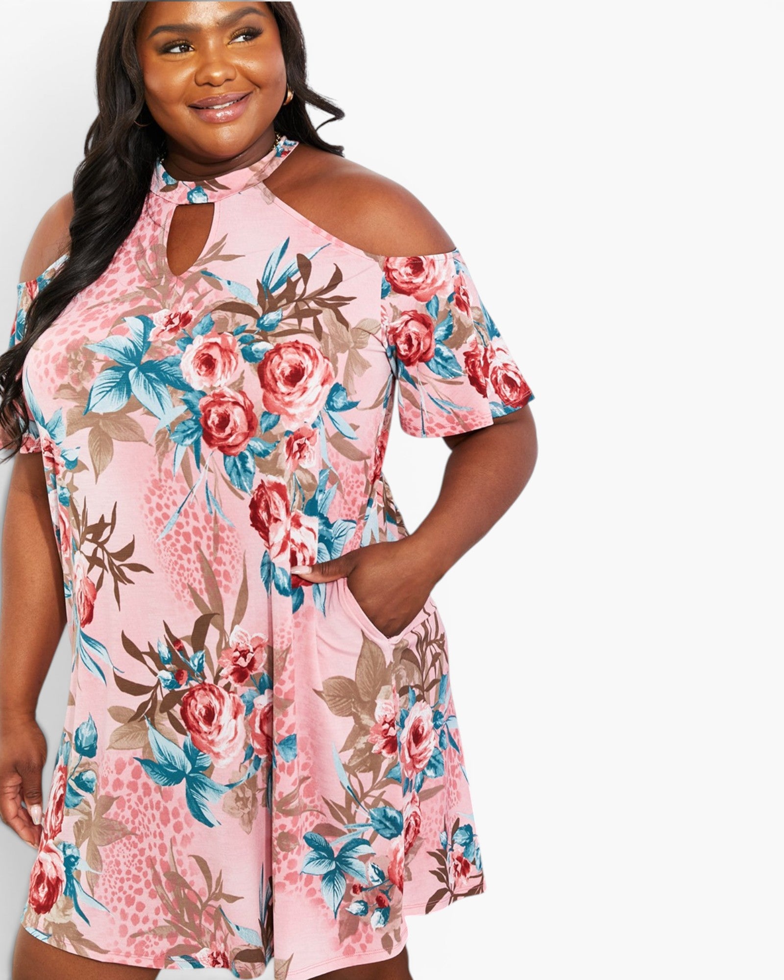 A plus-size woman wearing a pink cold-shoulder mini dress with a red, blue, and brown floral print, shown against a plain white background.