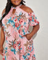 Woman wearing a floral dress with pink, blue, and red flowers on a plain background