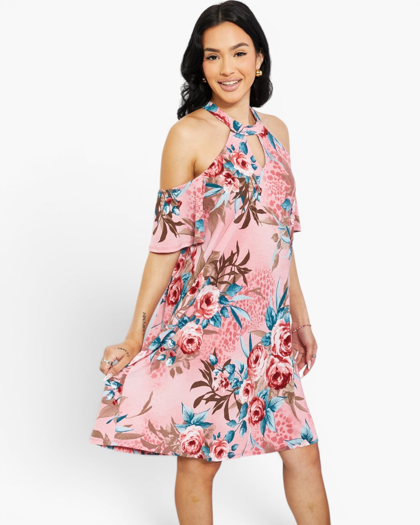 A woman modeling a pink cold-shoulder floral dress with blue, red, and brown botanical print against a plain white studio background.