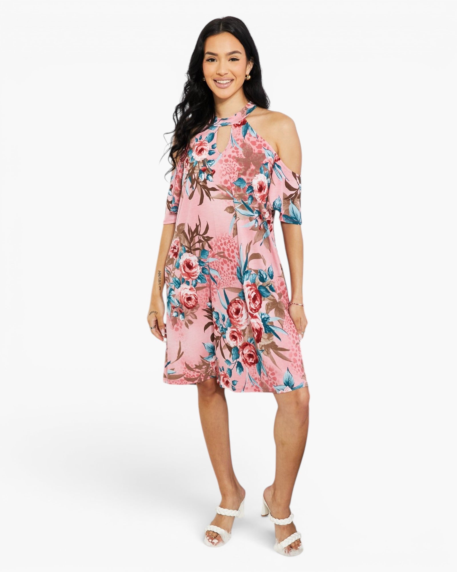 A woman modeling a pink floral cold-shoulder dress with blue and red accents, paired with white heeled sandals, against a plain white studio background.