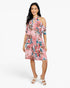 A woman modeling a pink floral cold-shoulder dress with blue and red accents, paired with white heeled sandals, against a plain white studio background.