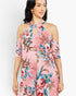 A woman wearing a pink cold-shoulder floral dress with blue, red, and brown botanical print details, shown against a plain light gray studio background.