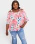 Woman wearing a pink floral off-shoulder top and blue jeans on a white background