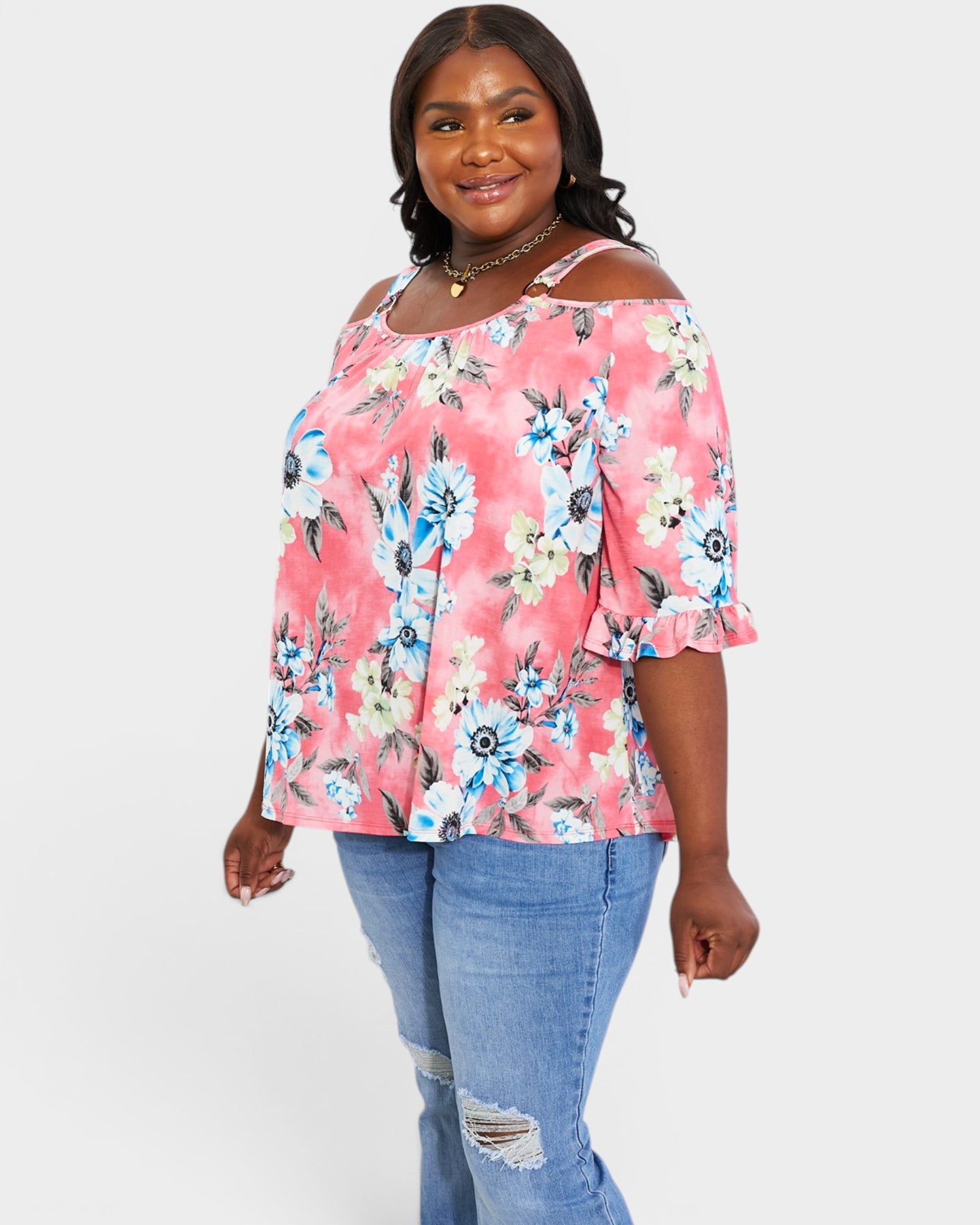 Woman wearing a pink floral off-shoulder top and blue jeans on a white background