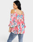 Woman wearing a pink floral off-shoulder top and jeans on a white background