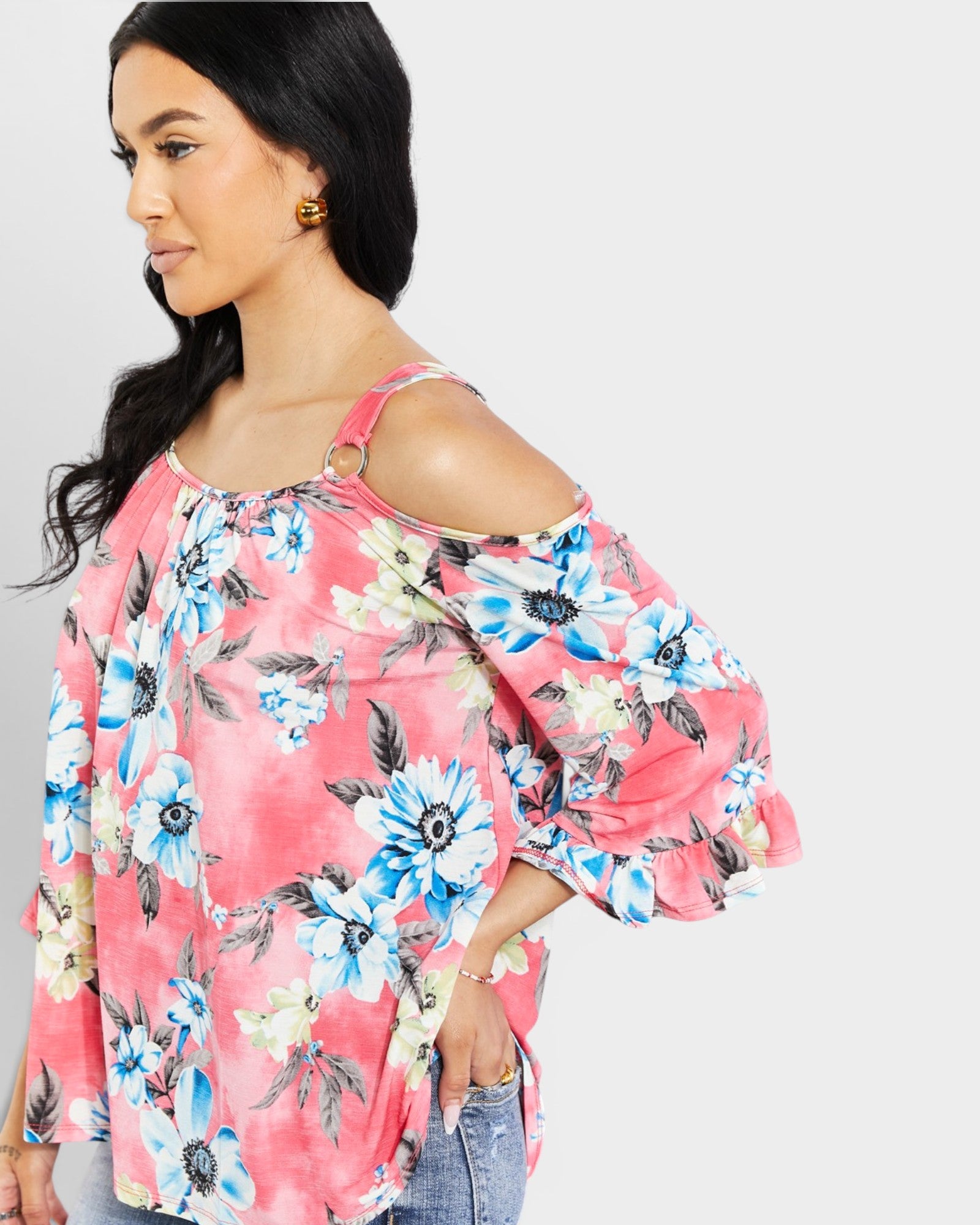 Woman wearing a pink floral blouse with cut-out shoulders on a plain background