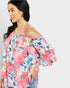 Woman wearing a pink floral blouse with cut-out shoulders on a plain background