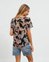 Woman wearing a black patterned top and denim shorts on a white background