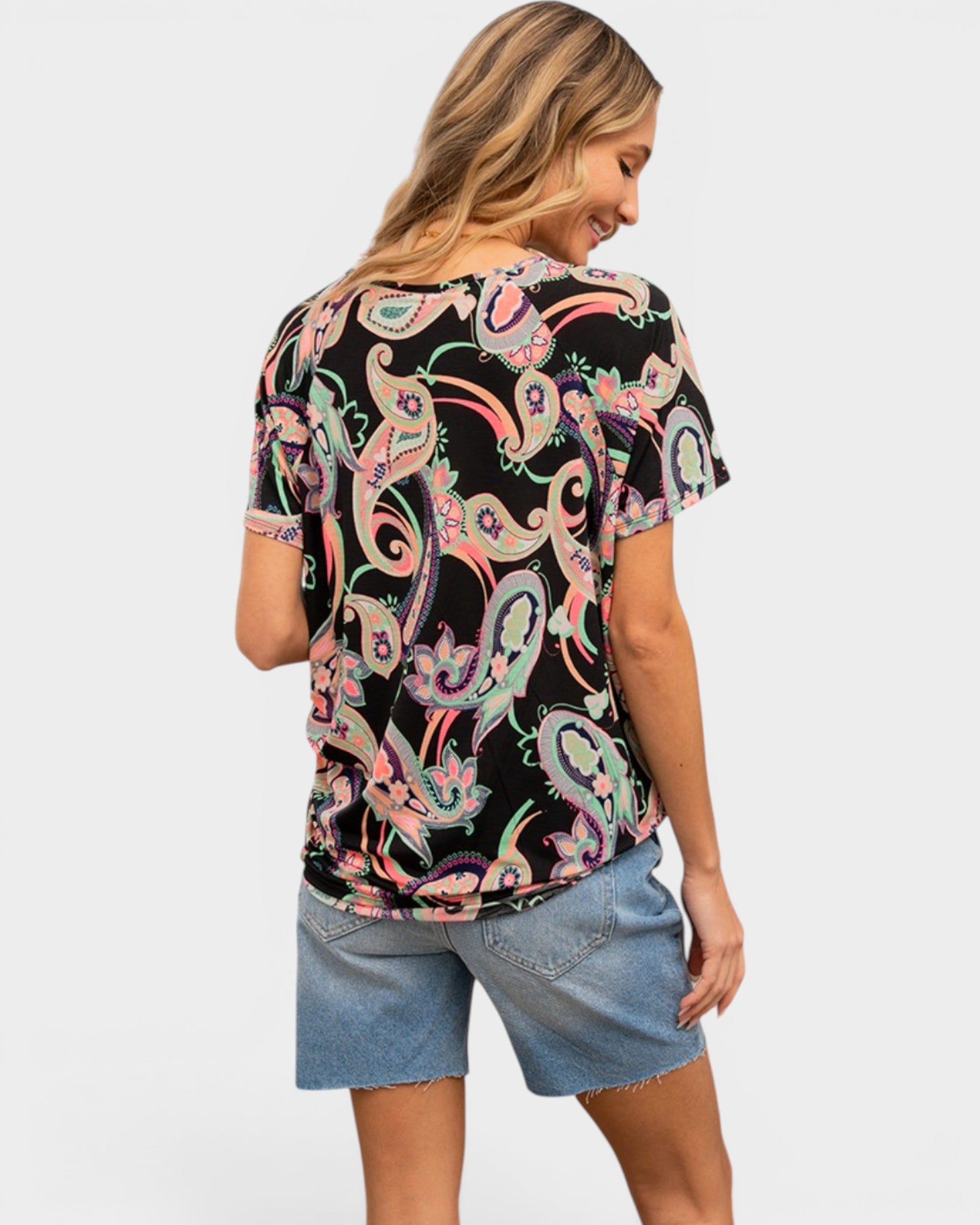 Woman wearing a black t-shirt with colorful paisley pattern and denim shorts on a white background