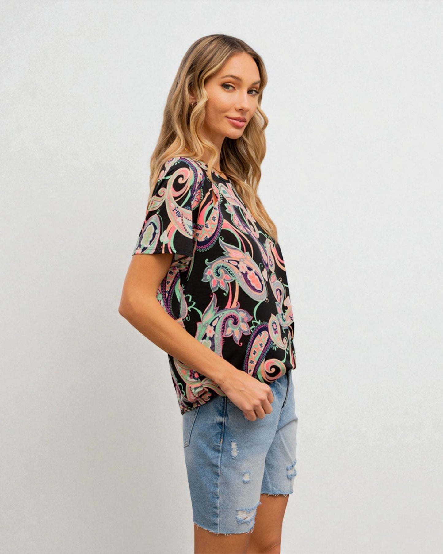Woman wearing a patterned top and denim shorts on a plain background
