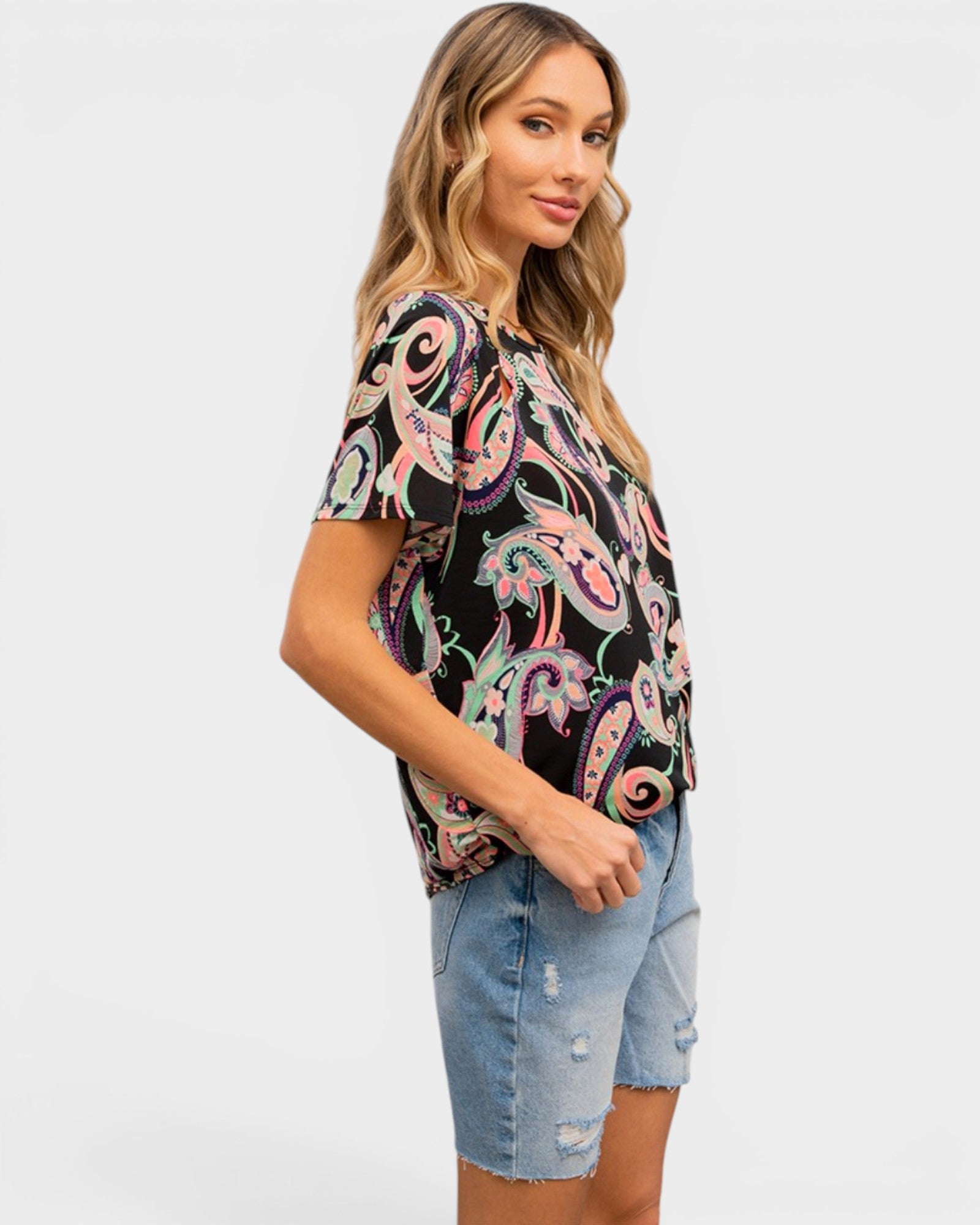 Woman wearing a colorful paisley top and denim shorts on a white background