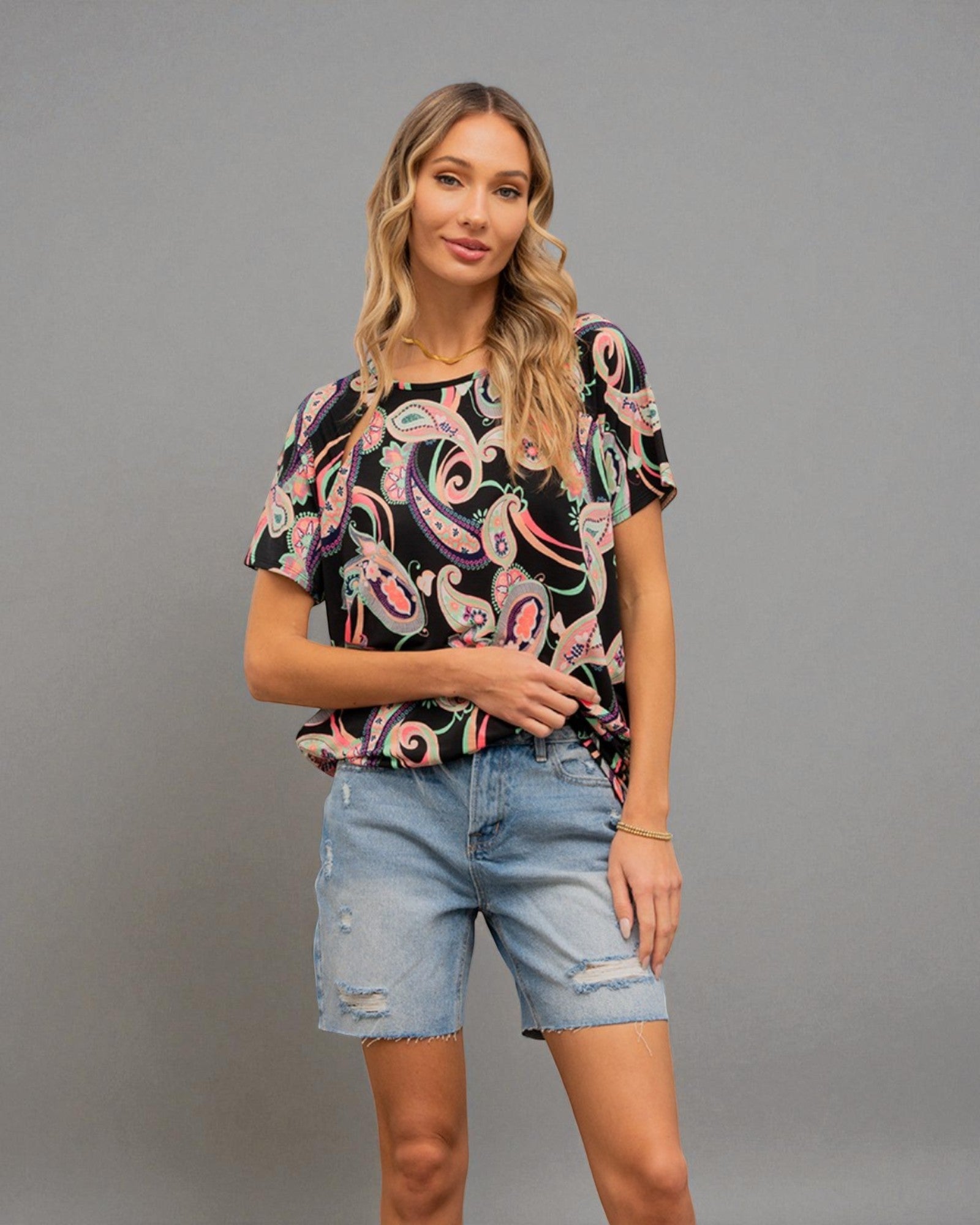 Woman wearing a black patterned top and denim shorts on a gray background