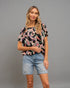 Woman wearing a black patterned top and denim shorts on a gray background