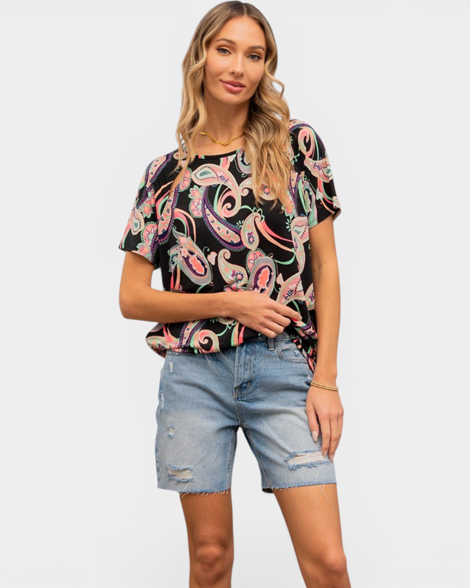 Woman wearing a patterned black top and denim shorts on a white background