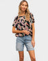 Woman wearing a patterned black top and denim shorts on a white background