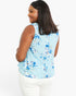 A woman shown from the back wearing a sleeveless light blue top with a blue and white floral pattern, paired with white pants, against a plain white background.