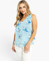 A woman wearing a light blue sleeveless blouse with a blue and white floral pattern, paired with white pants, photographed against a plain white studio background.