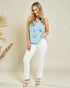 Woman wearing a light blue floral sleeveless top and white pants against a beige background