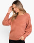 A woman wearing a textured knit sweater in a dusty rose color, paired with black pants, against a plain white background.
