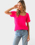 Woman wearing a bright pink textured top and light blue jeans on a white background