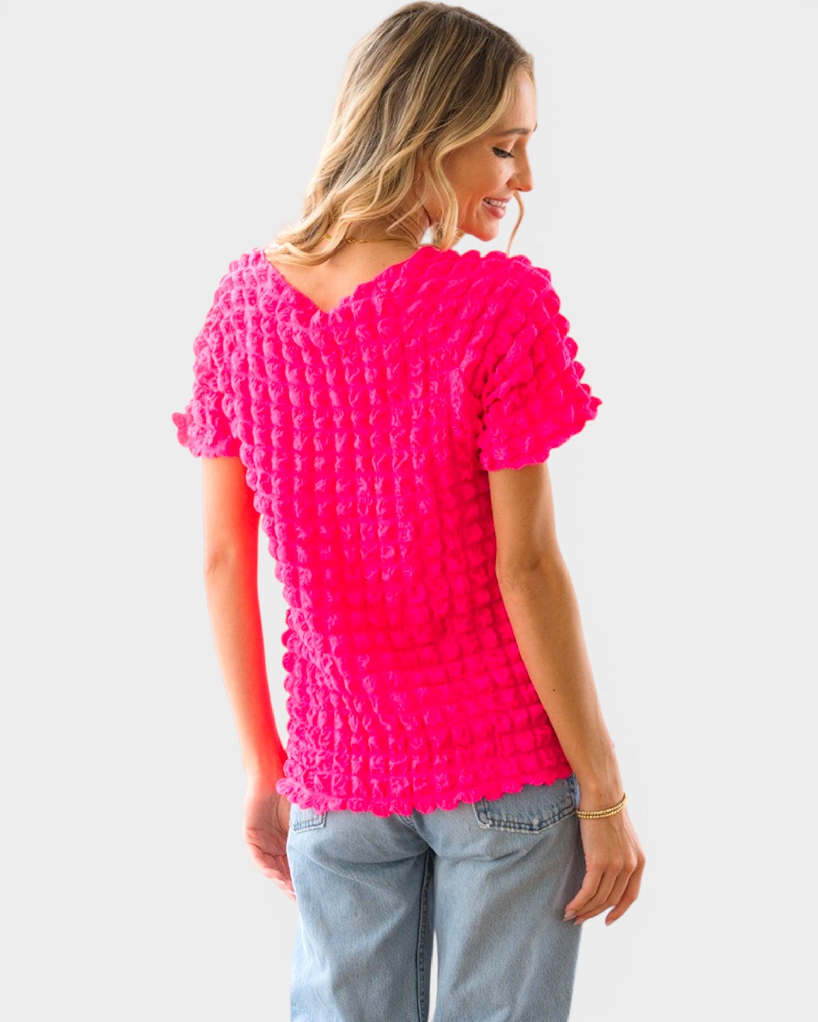 Woman wearing a bright pink textured top and light blue jeans on a white background