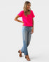Woman wearing a bright pink textured top and blue jeans on a white background