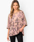 A woman modeling a loose, short-sleeve top with a pink and taupe geometric tribal pattern, paired with black pants, against a light gray studio background.