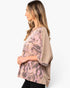 A woman shown in side profile wearing a loose, short-sleeve top with a pink and taupe geometric pattern on a solid taupe base, photographed against a clean white background.