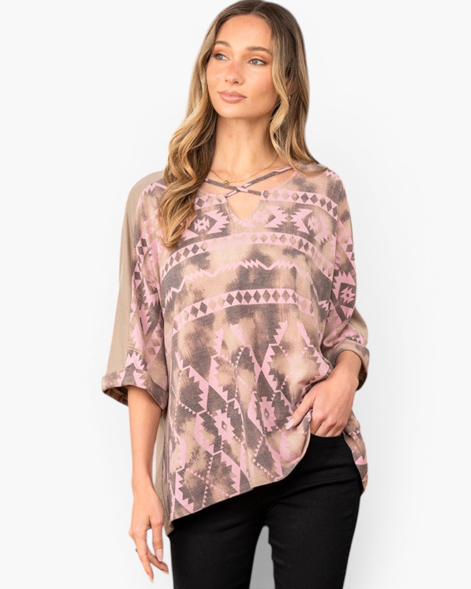 A woman wearing a loose, short-sleeve top with a pink, brown, and beige geometric tribal pattern and a keyhole cutout at the neckline, paired with black pants, against a plain white background.