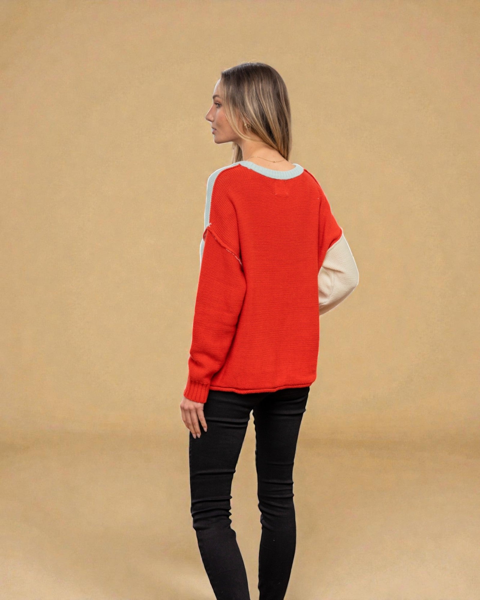 Woman wearing a red sweater with a beige shirt underneath on a beige background