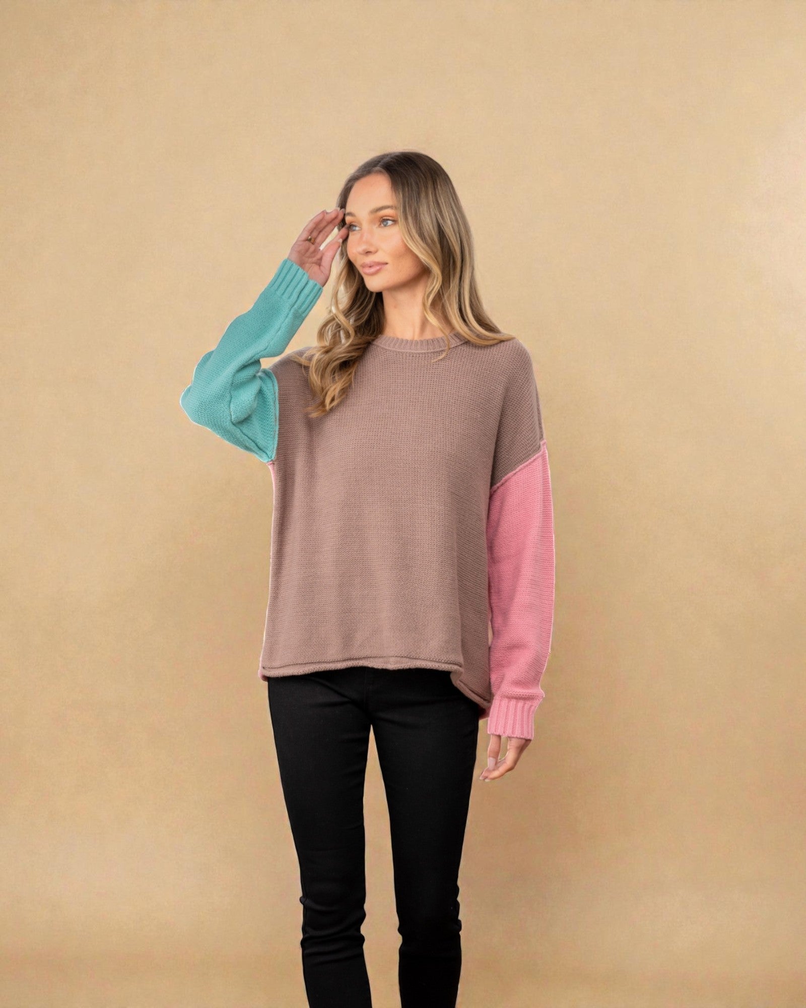 Woman wearing a sweater with color-blocked sleeves on a beige background