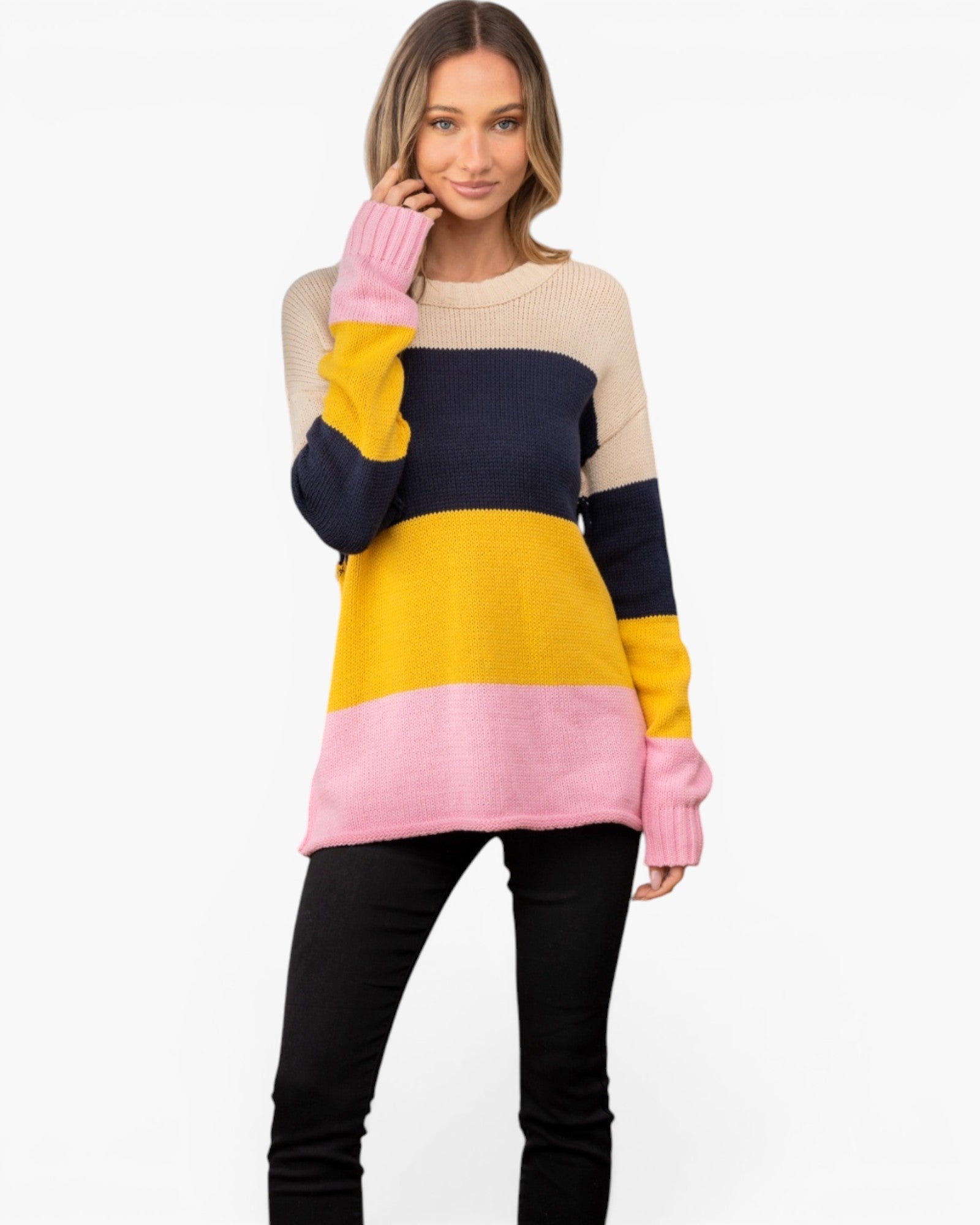 A woman modeling a color-blocked knit sweater with horizontal stripes of beige, navy, yellow, and pink, paired with black pants against a plain white background.