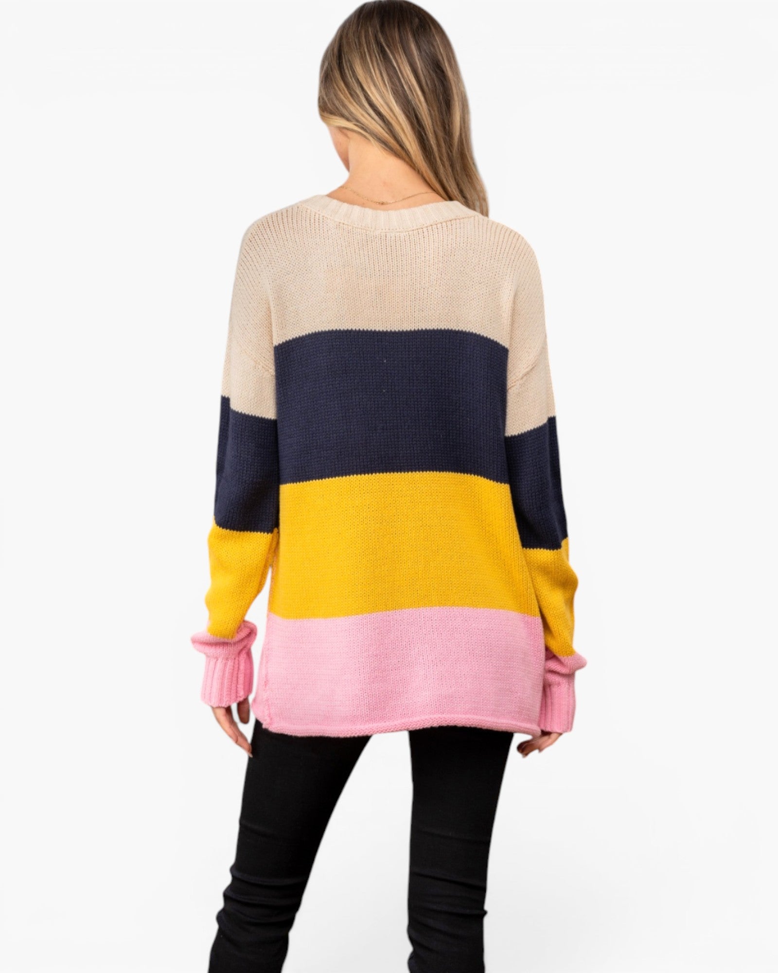 A woman shown from the back wearing a color-block knit sweater with horizontal stripes in beige, navy, yellow, and pink, paired with black pants, against a plain white background.