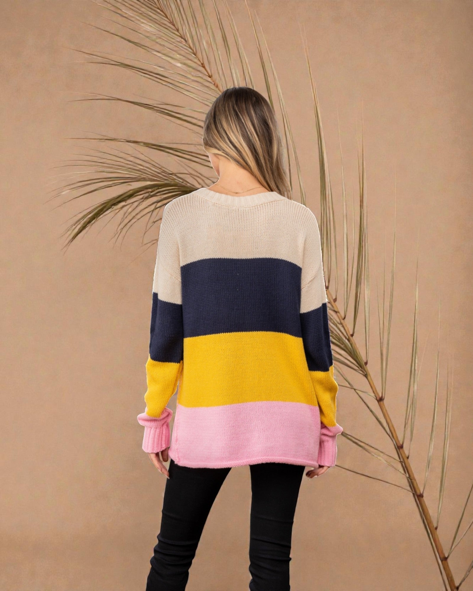 Woman wearing a color-blocked sweater with a beige, navy, yellow, and pink design against a beige background.