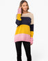 A woman modeling a color-blocked knit sweater with horizontal stripes of pink, yellow, navy, and beige, paired with black pants against a plain white background.