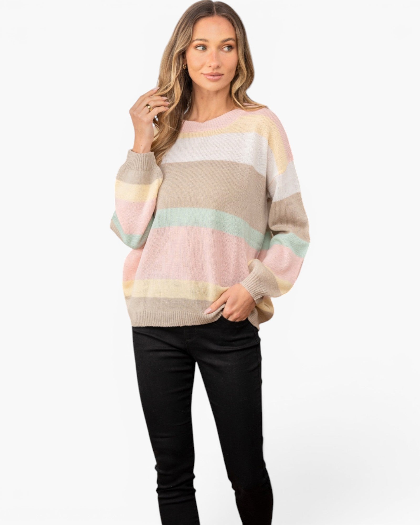 A woman modeling a pastel striped knit sweater with horizontal bands of pink, beige, cream, and mint green, paired with black pants, against a plain white background.
