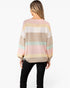 A woman shown from the back wearing a pastel striped knit sweater with black pants, photographed against a plain light gray studio background.