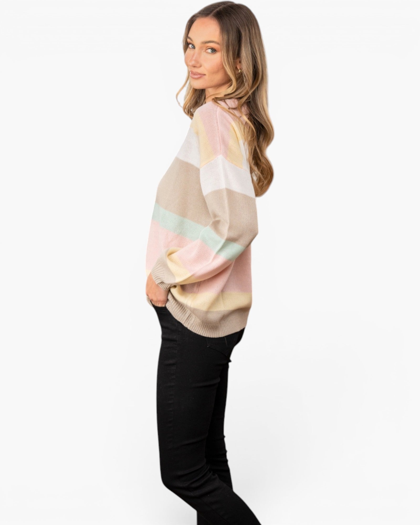 A woman wearing a pastel striped long-sleeve top with black pants, standing against a plain white studio background.