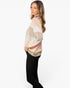 A woman wearing a pastel striped long-sleeve top with black pants, standing against a plain white studio background.