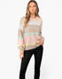 A woman modeling a pastel striped knit sweater with black pants against a plain white studio background.