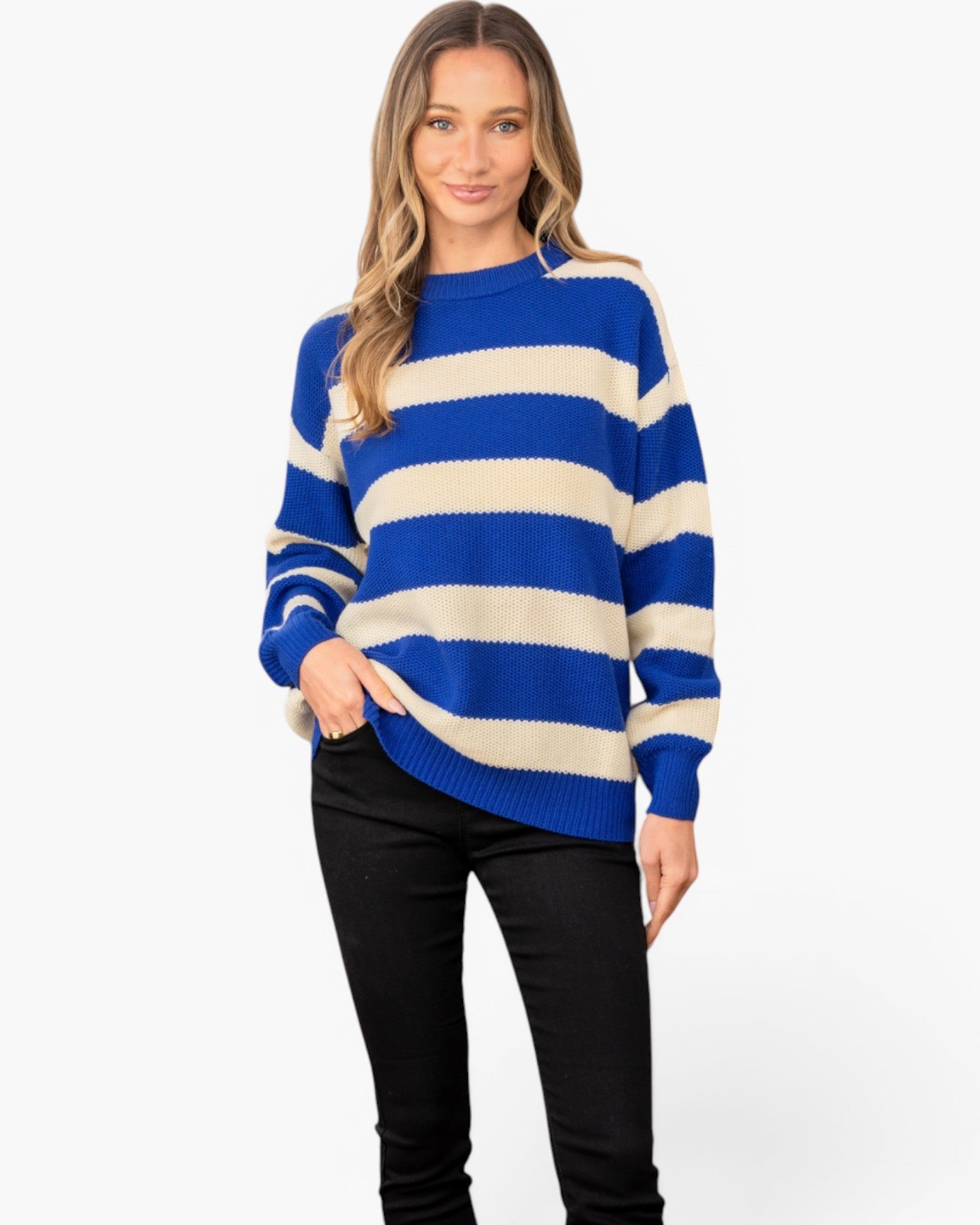 A woman modeling a blue and cream striped knit sweater with black pants against a plain white studio background.