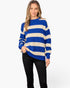 A woman modeling a blue and cream striped knit sweater with black pants against a plain white studio background.