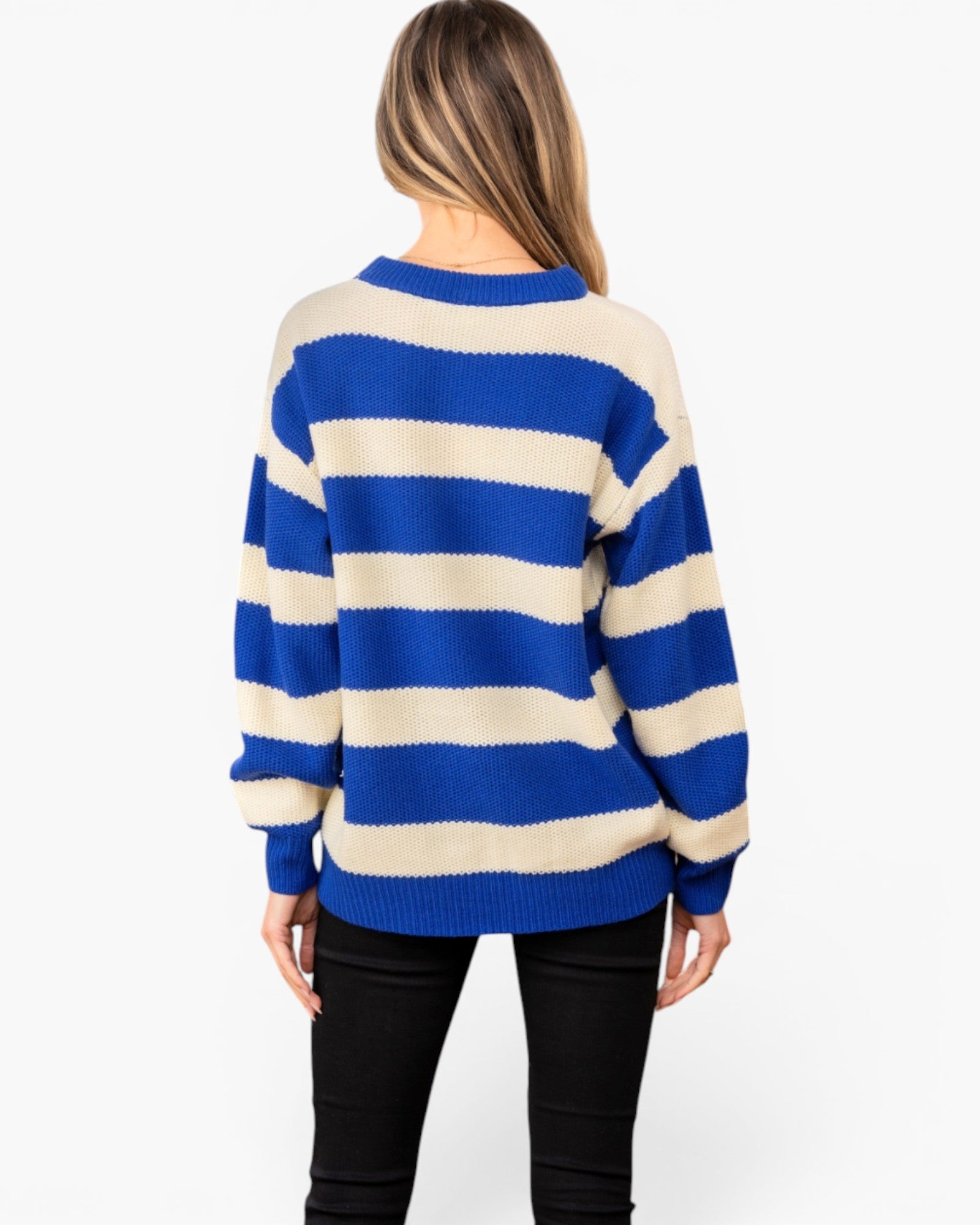 A woman viewed from the back wearing a blue and cream striped knit sweater and black pants, against a plain light gray studio background.