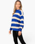 A woman modeling a blue and cream striped knit sweater with black pants, standing against a plain white studio background.