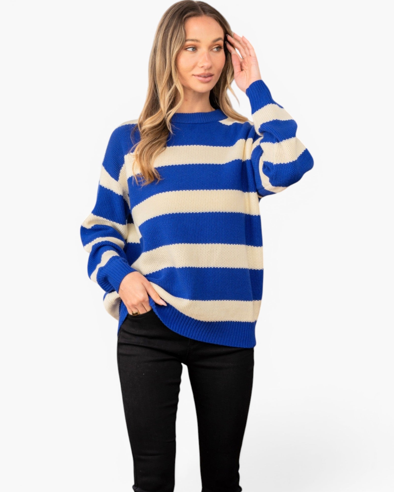 A woman modeling a blue and cream striped knit sweater with black pants against a plain white studio background.